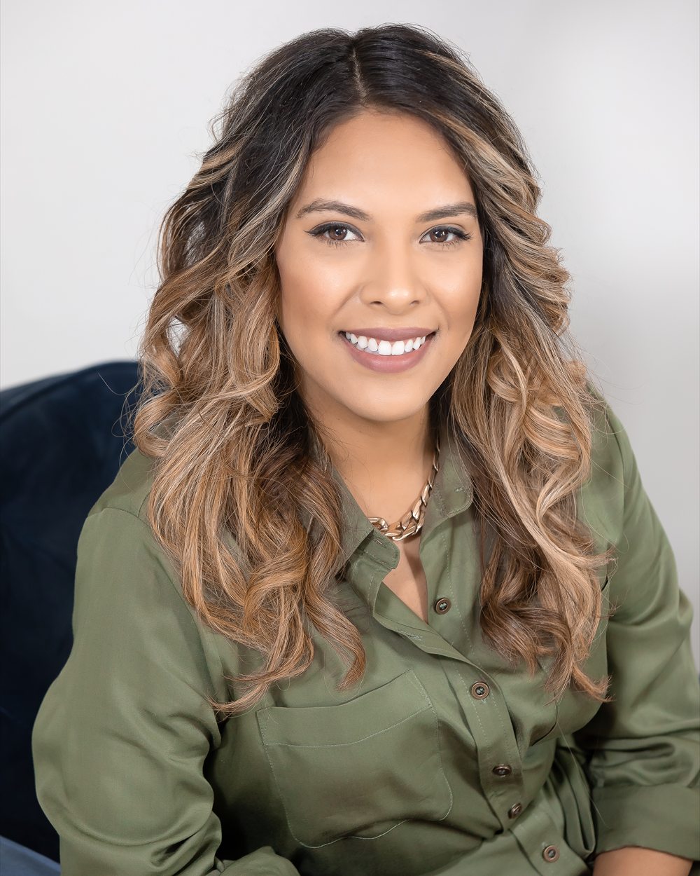 Maria, founder of Hearth & Kin, smiling in an olive-green shirt against a soft grey background.